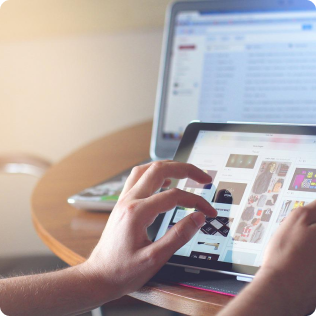 A person using a tablet and laptop on a table.